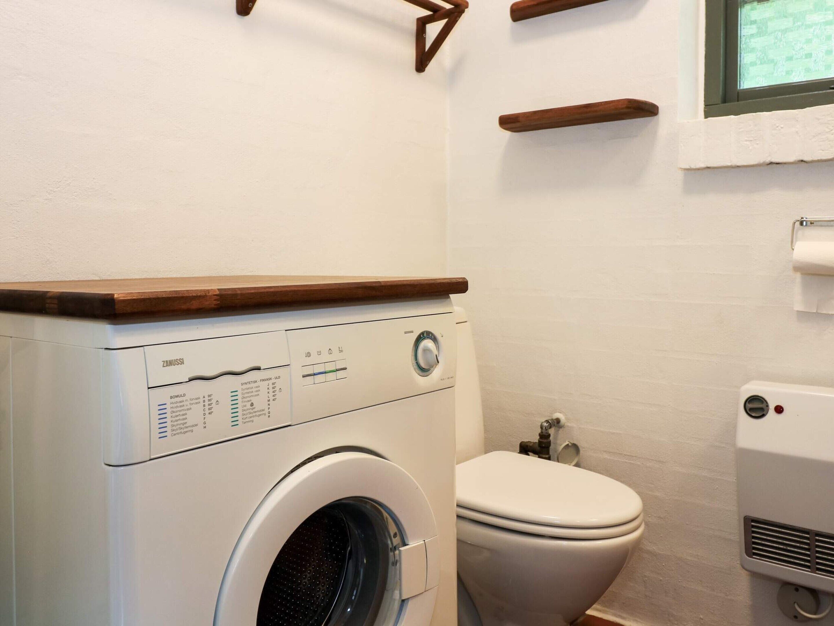 A compact bathroom with a washing machine, toilet, and a small window.