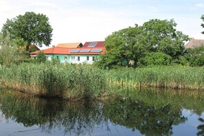 A house with a red roof, solar panels, and surrounded by dense greenery and a body of water. - Holiday home in Priborn with swimming pool (Priborn)
