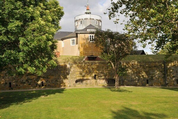 Ein historisches Gebäude mit einem runden Turm, Steinmauern und einem grünen Innenhof.