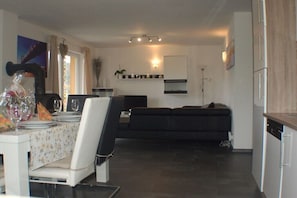 Eine moderne Küche mit Essbereich, einem schwarzen Sofa und einem weißen Esstisch mit Stühlen.