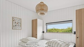 A bedroom with a bed, a window with a view, a hanging light fixture, and a framed picture on the wall. - 4 Star Holiday Home in Allinge (Allinge)