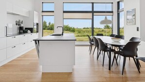 A modern kitchen with white cabinetry, a central island, and a dining area with black chairs and a table. - 4 Star Holiday Home in Allinge (Allinge)