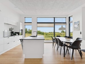 Una cocina moderna con muebles blancos, una isla central y un comedor con sillas negras y una mesa.