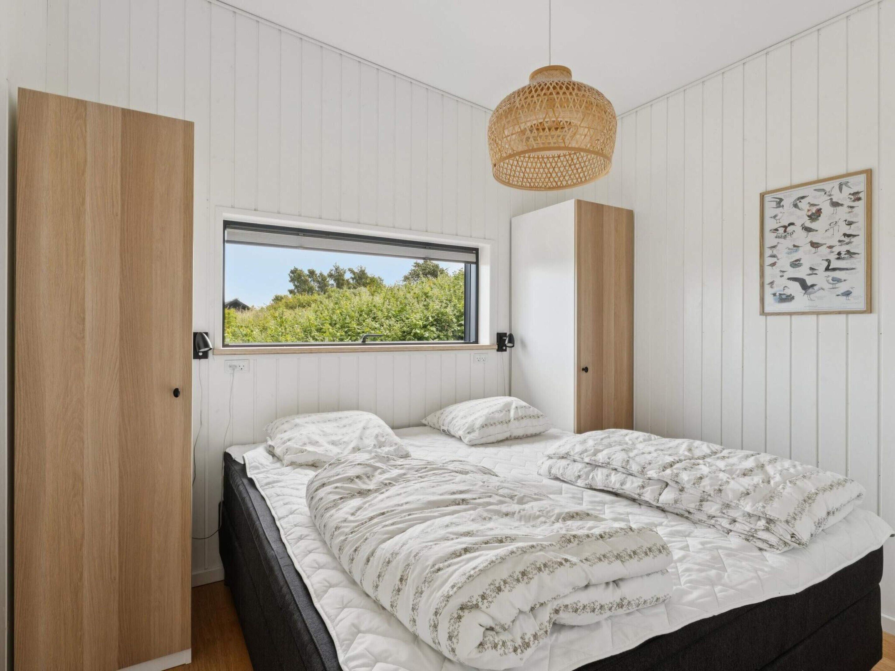 Quarto com cama, janela, luminária na parede e quadro com pássaros.