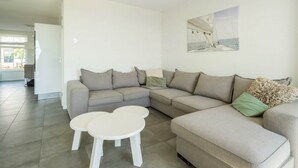 A modern living room with a sectional sofa, two white coffee tables, and a painting on the wall. - Westertoren Sauna 12 (Uitdam)