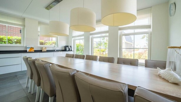 A modern kitchen with a long dining table, pendant lights, and large windows. - Westertoren Sauna 12 (Uitdam)