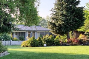 Une maison avec un toit en tuiles, entourée d’une pelouse bien entretenue et de divers arbustes.