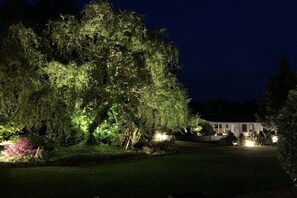 Ein Haus umgeben von Bäumen, beleuchtet durch Gartenleuchten bei Nacht.