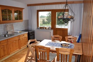 Eine Küche mit Holzausstattung, einem Esstisch mit Stühlen, einer Pendelleuchte und einem Fenster mit Vorhängen.