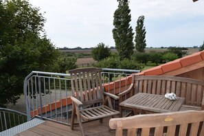 Eine Holterrasse mit Stühlen und einem Tisch, mit Blick auf eine ländliche Landschaft.