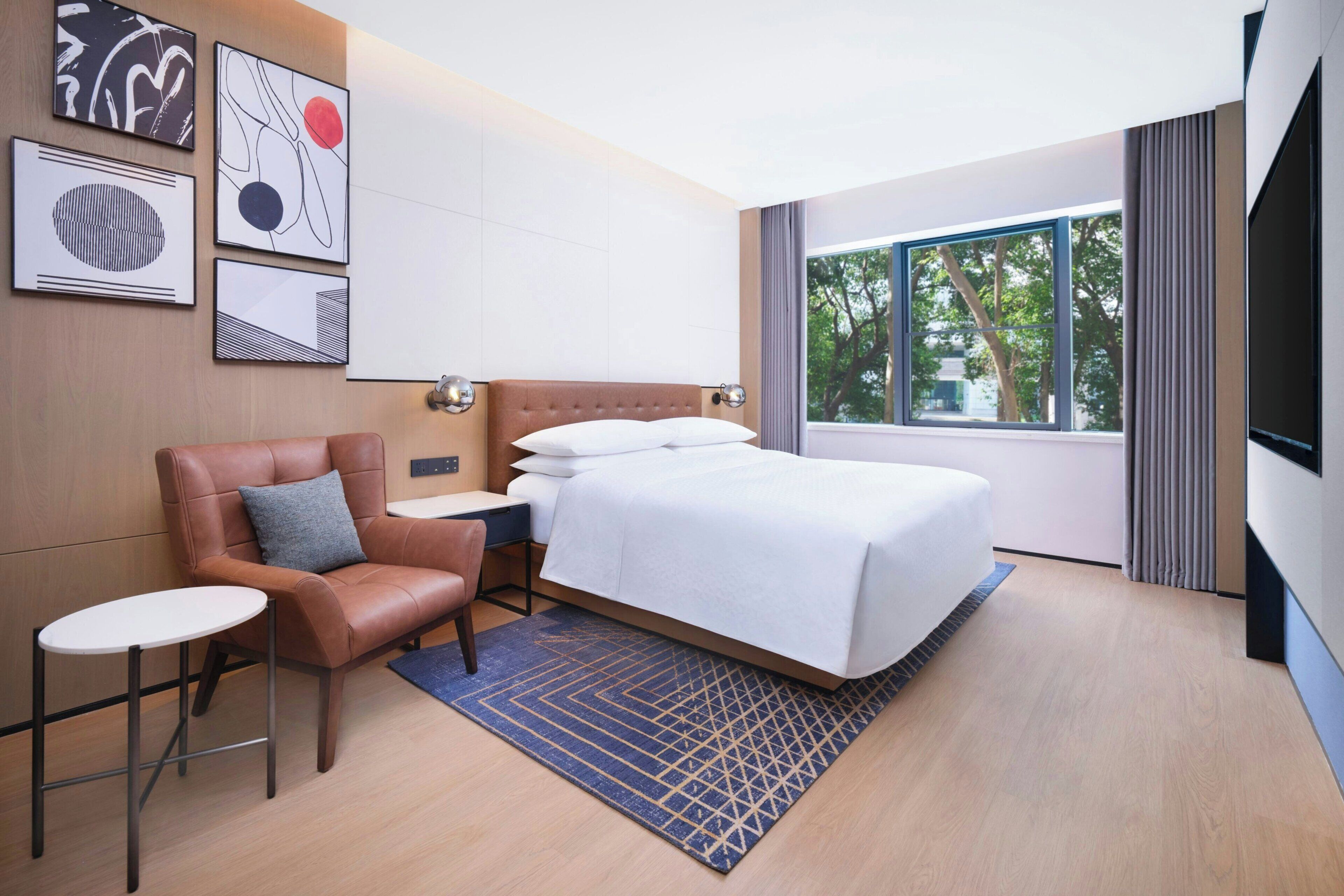 Una habitación de hotel con una cama, una silla, una mesita y obras de arte en la pared.