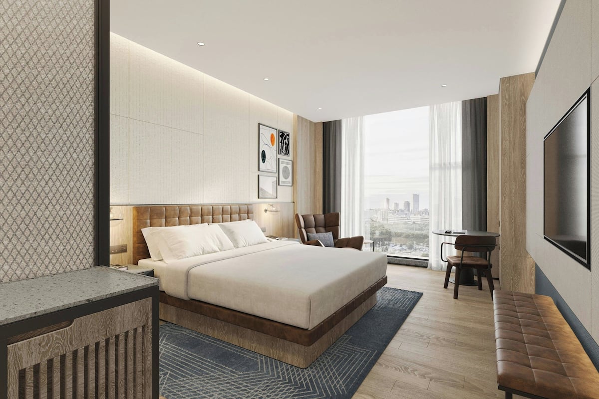 Une chambre moderne avec un grand lit, un bureau, une chaise, une télévision et une vue sur la ville.