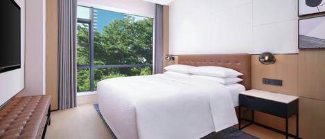 A hotel room with a large bed, a bench, a desk, and a TV.