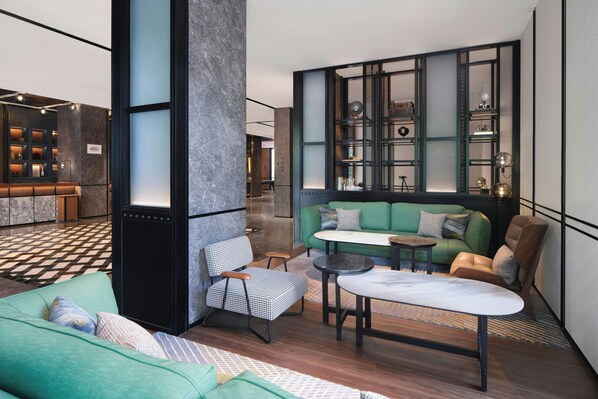 A modern interior with a green sofa, a houndstooth chair, and a small round table.