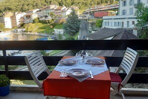 Ein Balkon mit Tisch für zwei Personen, mit Blick auf eine Stadt, in der Gebäude und eine Brücke zu sehen sind.