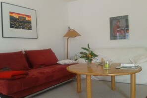 Ein Wohnzimmer mit einem roten Sofa, einem Holztisch, einer Stehlampe, einem Plakat und einer kleinen Pflanze.