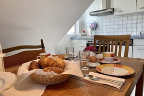 A breakfast setup with croissants, eggs, and beverages on a wooden table in a kitchen with white tiles and a window. - Holiday apartment with 2 bedrooms (Tönning)