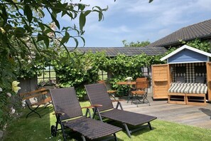 A patio with two lounge chairs, a wooden table, and a small seating area with a checkered cushion. - Holiday apartment with 2 bedrooms (Tönning)