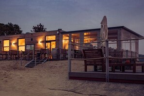 Ein Gebäude direkt am Strand mit Holzfassade, großen Fenstern und einer Treppe zum Eingang.