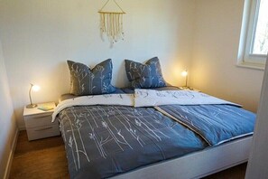 A bedroom with a bed, two bedside tables, a hanging light fixture, and a window. - Holiday home Sonnenufer (Dorf Zechlin  Ortsteil Beckersmühle)