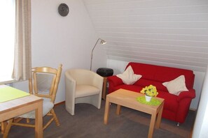 A small living area with a red sofa, a wooden chair, a small table, and a lamp. - North in the House Maria (Norderney)