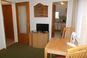 A room with a wooden dining table, a television on a stand, a cabinet, and a kitchen in the background. - North in the House Maria (Norderney)
