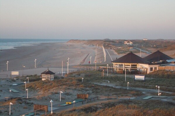 A coastal area with a beach, a boardwalk, and several buildings, including a pavilion and a house. - North in the House Maria (Norderney)