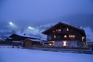 A large wooden building with multiple windows and balconies, surrounded by snow-covered ground and hills. - Apartment in Bramberg with barbecue (Bramberg)