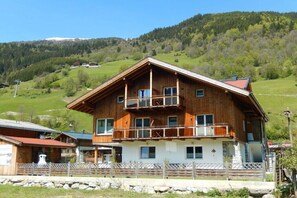 A wooden chalet with a balcony, set against a mountainous backdrop. - Apartment in Bramberg with barbecue (Bramberg)