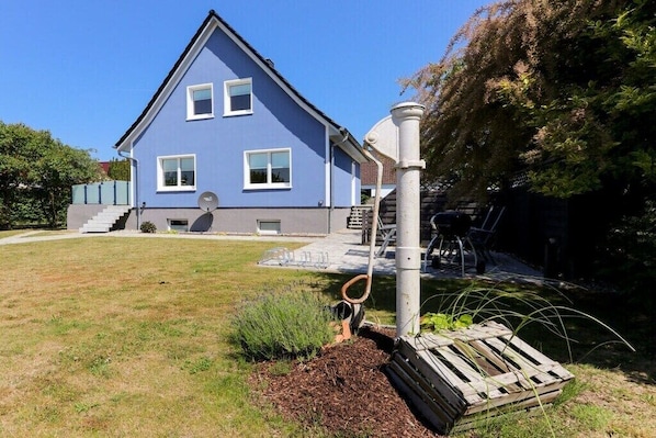 A two-story house with a blue exterior, a visible satellite dish, and a small garden area with a wooden pallet and mulch. - 2 Zeitke "the Little One" (Altefähr)
