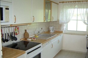 A kitchen with white cabinets, a microwave, a stove, a sink, and a window with curtains. - in the Bergblick house (Annaberg-Buchholz OT Cunersdorf)