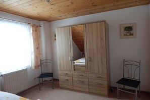 A bedroom with a wooden wardrobe, two metal chairs, a radiator, and a window with curtains. - in the Bergblick house (Annaberg-Buchholz OT Cunersdorf)
