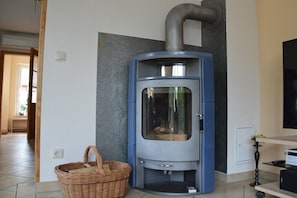 Ein Eckzimmer mit eingebautem Holzofen, einem Korbwäschesessel und einem Flachbildfernseher.