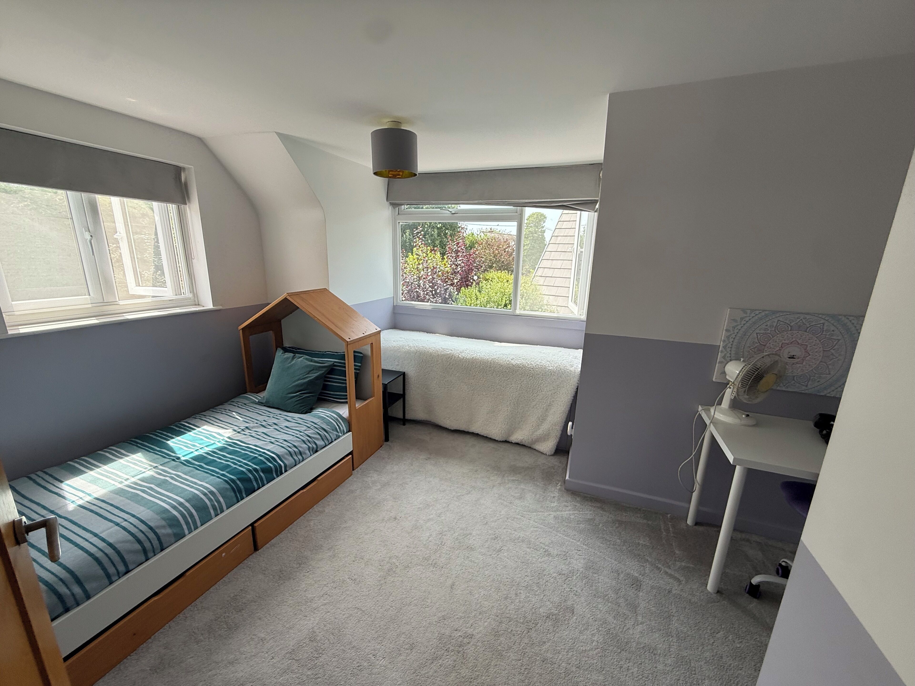 Une petite pièce comprenant un lit superposé, un bureau et une fenêtre donnant sur un espace verdoyant.