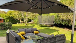 Een patio met een wickerbank, een tafel met glazen blad en een grote parasol.
