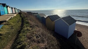 Een rij strandhutten langs een begroeiing pad aan de zee, met de oceaan en een heldere lucht op de achtergrond.
