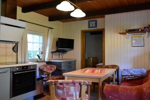 Eine kleine Küche mit Herd, Backofen und einem Fernseher auf einem Schrank. Ein Essbereich mit Tisch und Stühlen sowie ein rotes Sofa sind ebenfalls vorhanden.