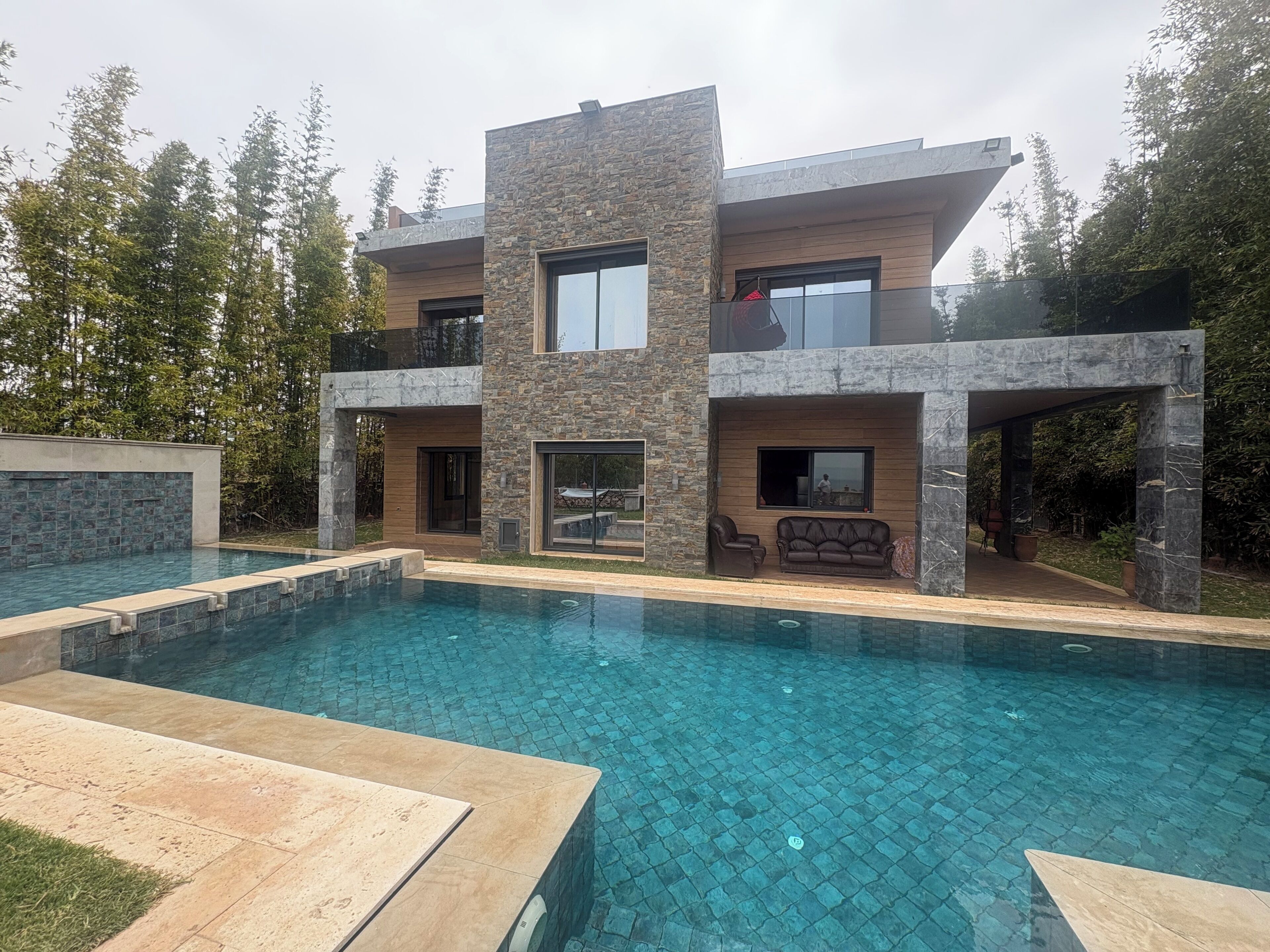 Une maison moderne à plusieurs étages, dotée d’une piscine, d’une façade en pierre et d’un espace extérieur aménagé pour se détendre.