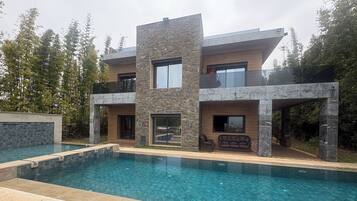 A modern multi-story house with a swimming pool, stone facade, and outdoor seating area.