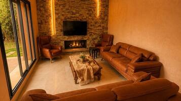 A modern living room with a stone wall, leather sofas, a flat-screen TV, and a fireplace.