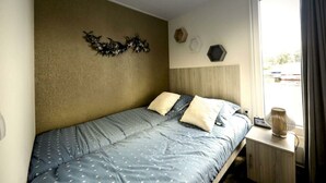 A bedroom with a bed, a nightstand, a wall-mounted lamp, and a window with curtains. - Holiday Home in Olburgen With Terrace (Olburgen)