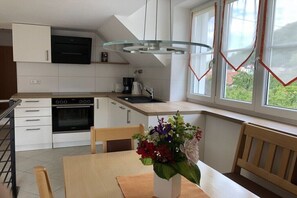 Una cocina moderna con armarios blancos, horno empotrado y una zona de comedor con mesa y sillas.