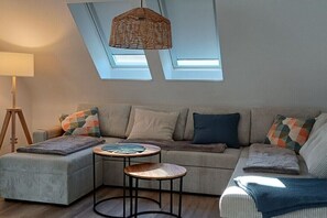 Ein Wohnzimmer mit einer Couch, zwei kleinen Tischen, einer Lampe und einer Deckenleuchte.