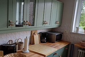 Eine Küche mit grünen Schränken, einer Holzausziehtisch, einem Toaster, einer Kaffeemaschine und einer Mikrowelle.