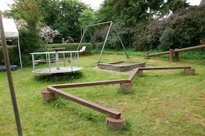 Ein Spielplatz mit Schaukeln, einer Wippe und einer runden Kletterkonstruktion.