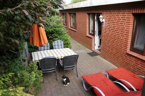 Eine Terrasse mit Tisch und Stühlen, ein rot Backsteinhaus und eine Katze.