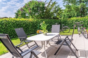 Eine Terrasse im Freien mit einem weißen Tisch, vier Stühlen, einem Topfpflanzen und einem Fahrrad im Hintergrund.