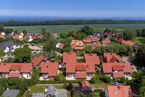 Ein Wohngebiet mit Häusern und roten Ziegeldächern, umgeben von viel Grün und einem großen Gewässer im Hintergrund.
