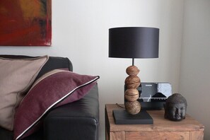 Ein modernes Wohnzimmer mit einem schwarzen Sofa, einem Holztisch, einer schwarzen Lampe, einer Buddha-Statue und einem roten abstrakten Gemälde an der Wand.