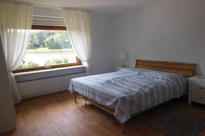 Ein Schlafzimmer mit Bett, einem Fenster mit Vorhängen, einem Nachttisch und einem Heizkörper.